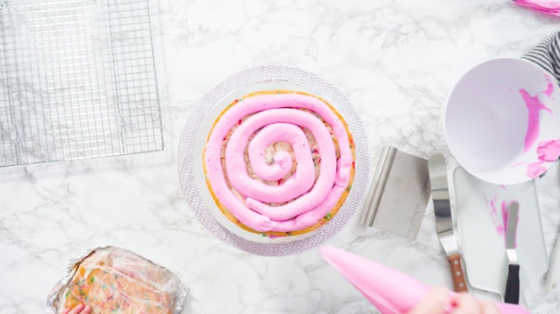 Mise à plat. Pas à pas. Glaçage des couches de gâteau funfetti rond avec un glaçage à la crème au beurre rose.