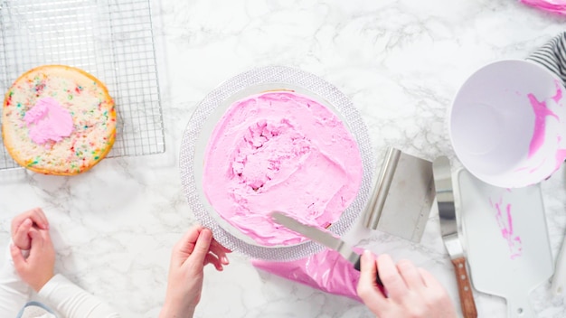 Mise à plat. Pas à pas. Glaçage des couches de gâteau funfetti rond avec un glaçage à la crème au beurre rose.