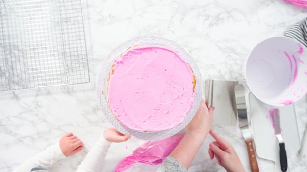 Mise à plat. Pas à pas. Glaçage des couches de gâteau funfetti rond avec un glaçage à la crème au beurre rose.