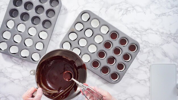 Mise à plat. Pas à pas. Répartir la pâte à cupcake dans des lignes de mini cupcakes pour cuire des mini cupcakes au chocolat.