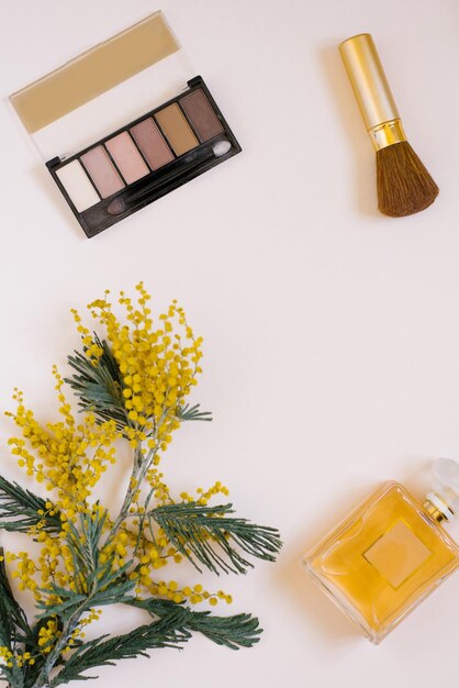 Mise à plat pour femmes à la mode avec un bouquet de fleurs de mimosa jaune et des ombres de parfum et un pinceau sur une table beige Concept de planification