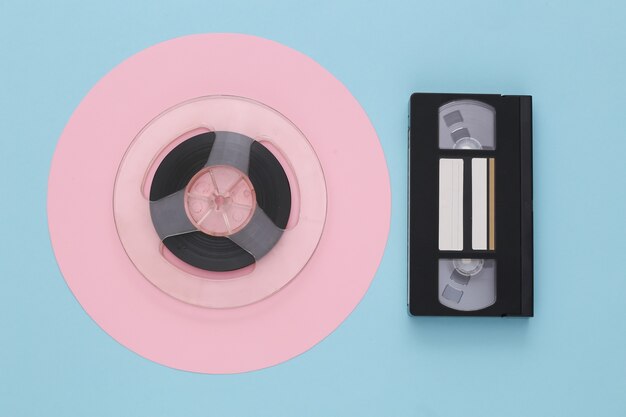 Mise à plat rétro. Bobine de bande magnétique audio et cassette vidéo sur pastel bleu rose