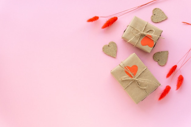 Mise à plat de la Saint-Valentin zéro déchet. Coffrets cadeaux emballés dans du papier kraft avec des coeurs et des épillets sur un mur rose.