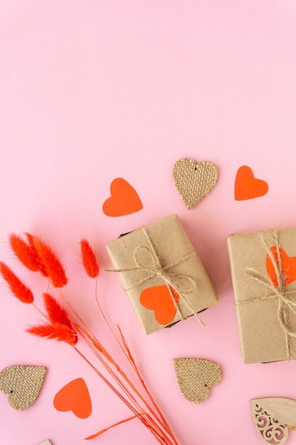 Mise à plat de la Saint-Valentin zéro déchet. Coffrets cadeaux emballés dans du papier kraft avec des coeurs et des épillets sur un mur rose.