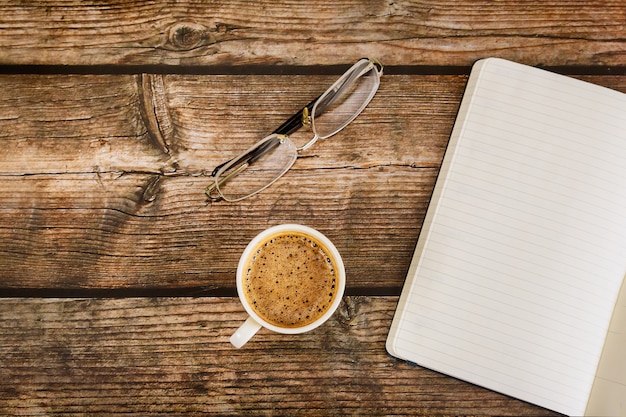 Mise à plat de table de bureau moderne avec page de cahier vierge dans une tasse de café sur bois