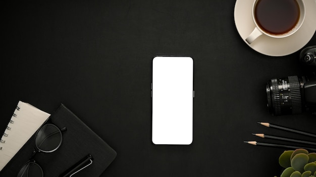 Mise à plat Une table de bureau noire moderne avec papeterie pour appareil photo et écran vierge pour smartphone
