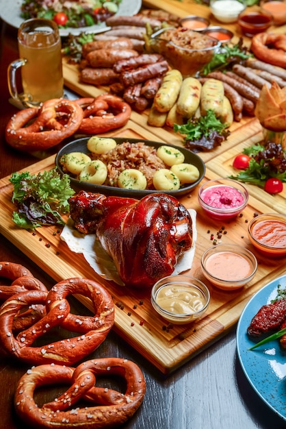 Mise à plat de la table du dîner de l'Oktoberfest avec des saucisses à la viande grillée, des bretzels, des pommes de terre, une salade de concombre, des sauces, des bières