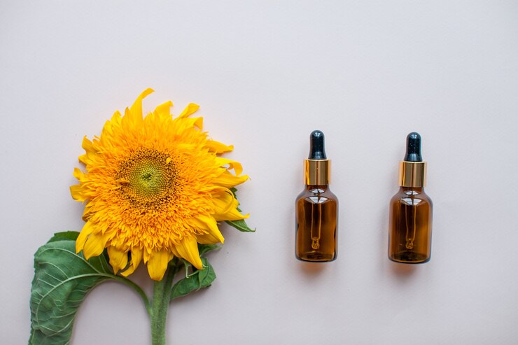 Mise à plat de tournesols et de bouteilles pour sérum ou crème cosmétique sur fond rose clair le