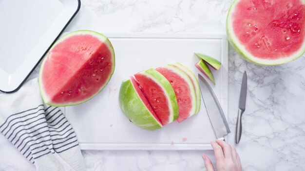 Mise à plat. Trancher la pastèque rouge en petits morceaux sur une planche à découper blanche.