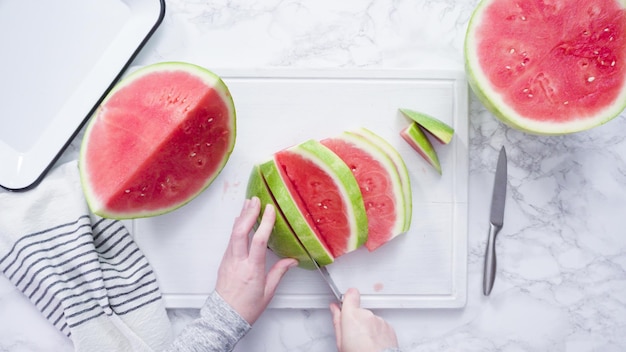 Mise à plat. Trancher la pastèque rouge en petits morceaux sur une planche à découper blanche.