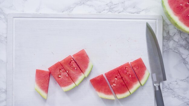 Mise à plat. Trancher la pastèque rouge en petits morceaux sur une planche à découper blanche.