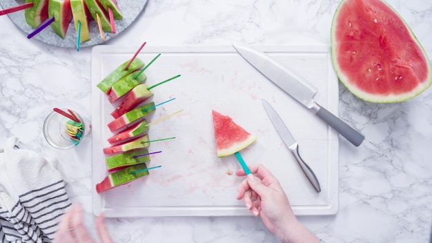 Mise à plat. Trancher la pastèque rouge en petits morceaux sur une planche à découper blanche.