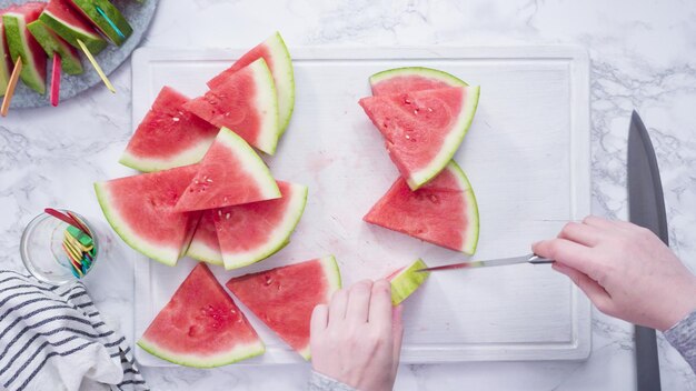 Mise à plat. Trancher la pastèque rouge en petits morceaux sur une planche à découper blanche.