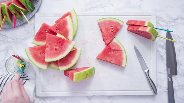 Mise à plat. Trancher la pastèque rouge en petits morceaux sur une planche à découper blanche.