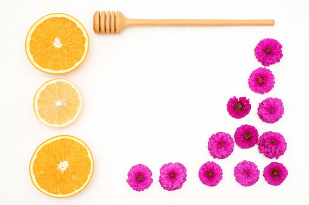 Une mise à plat de tranches de fruits orange avec des pétales d'orchidées rouges et une cuillère à miel en bois allongé sur un espace de copie de fond blanc