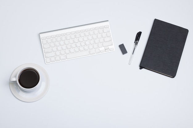 Photo mise à plat, vue de dessus bureau table de bureau moderne. livre noir café, stylo, crayon et clavier sur blanc