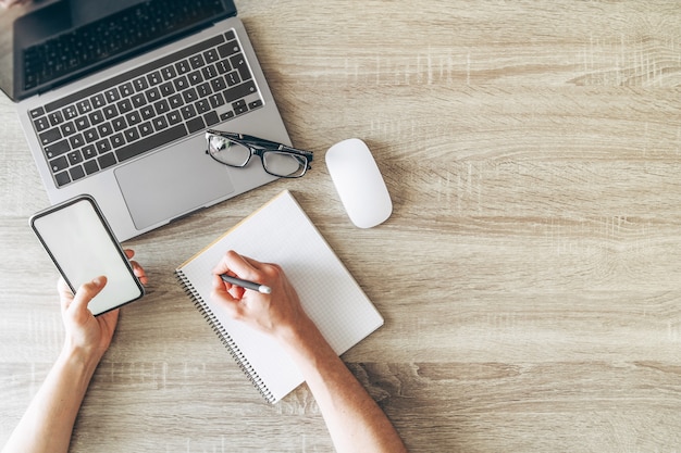 Mise à plat, vue de dessus de l'espace de travail du bureau avec ordinateur portable, mains, ordinateur portable et téléphone portableMise à plat, vue de dessus de l'espace de travail du bureau avec ordinateur portable, mains, ordinateur portable et téléphone portable.