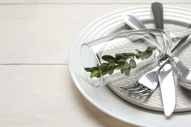 Mise en table. coutellerie. Fourchette, couteau, verre, cuillère et assiette sur une table en bois blanc.