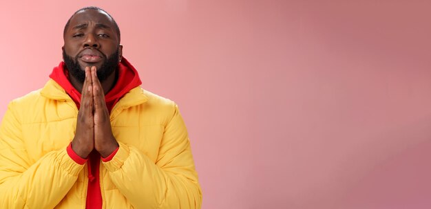 Photo misérable mignon afro-américain homme barbu en manteau jaune demandant de l'aide mendiant presse palms personne