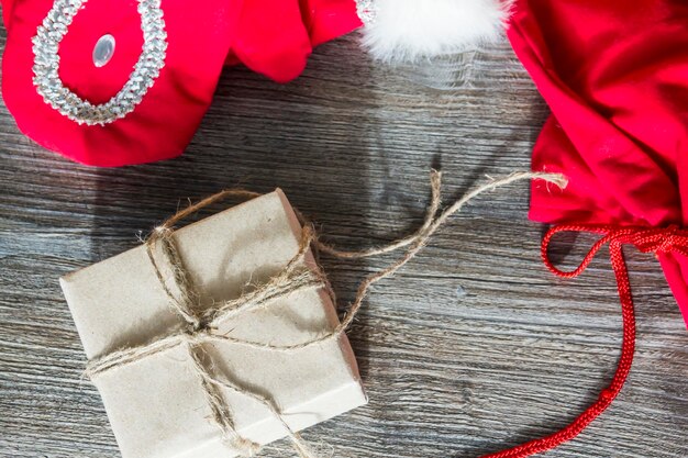 Mitaines rouges du Père Noël et une boîte avec des cadeaux dans un emballage artisanal sur une surface en bois