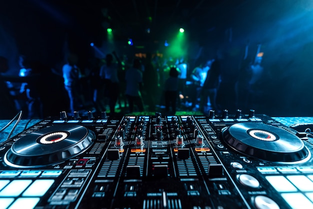 Photo mixeur de musique dj sur un stand dans une discothèque sur un arrière-plan flou des danseurs