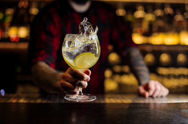 Mixologue tenant un verre à cocktail avec une boisson fraîche aux agrumes aigre-douce et sucrée avec des tranches de citron vert