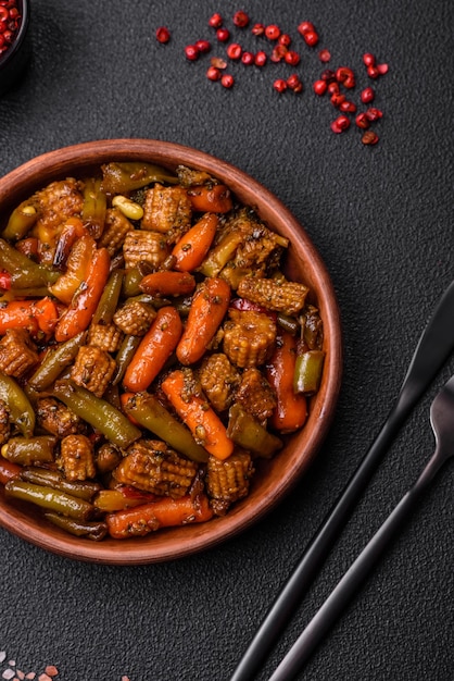 Mixture de légumes, de maïs, de carottes, de poivrons, de brocolis, d'oignons dans une sauce teriyaki sur une assiette en céramique sur un fond en béton sombre