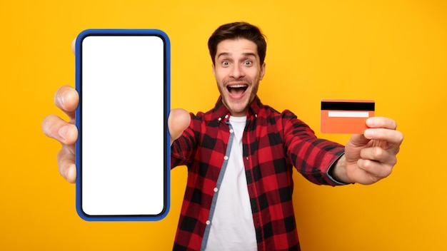 Mman excité montrant un écran de téléphone portable vierge et une carte de crédit