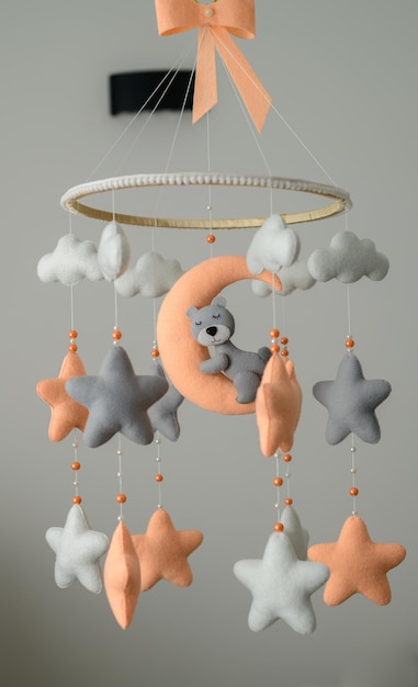 Mobile pour lit de bébé suspendu dans la chambre de la pépinière thème orange et gris pastel ours endormi sur la lune entouré d'étoiles