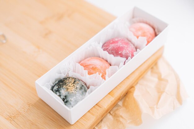 Photo des mochi colorés appétissants dans une boîte sur une planche en bois