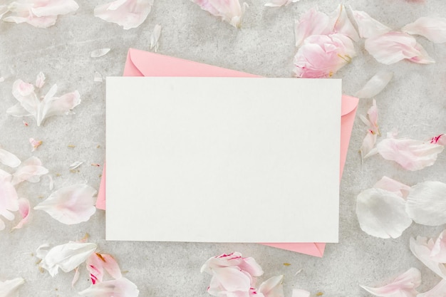 Mockup d'invitation carte de vœux en papier blanc enveloppe rose et pionnées sur une table en pierre grise fond de fleur vue supérieure plate