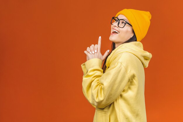 À la mode belle jeune caucasienne jeune étudiante portant des vêtements élégants en riant, en pointant le doigt. Isolé sur orange.