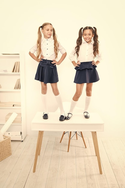 La mode de l'école primaire Les écoliers heureux avec la mode regardent debout sur la table La mode des petites filles avec de longs cheveux et des queues de cheval souriants en classe La mode pour les petits étudiants