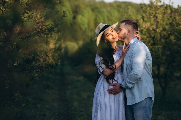 À la mode et élégante femme enceinte heureuse et son mari habillé d'un ton pastel blanc et bleu dans le jardin au coucher du soleil