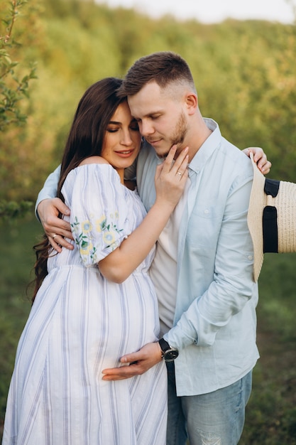 À la mode et élégante femme enceinte heureuse et son mari habillé d'un ton pastel blanc et bleu dans le jardin au coucher du soleil