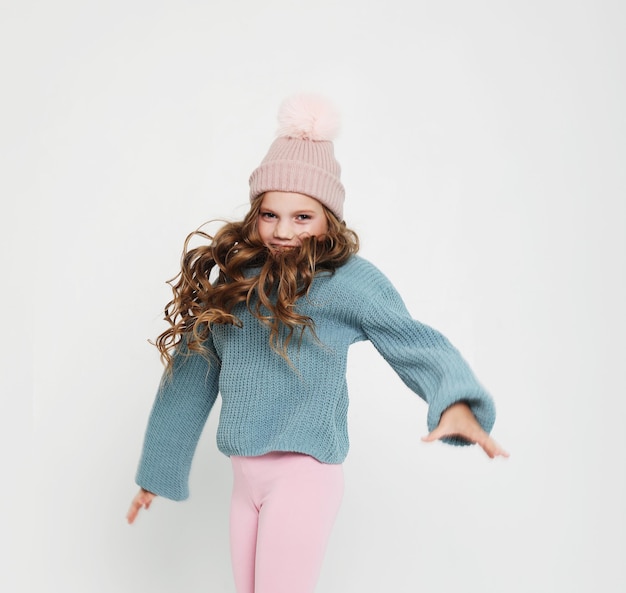 Mode enfantine et concept de personnes Petite fille au chapeau rose et pull bleu sautant sur fond blanc