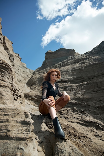 Mode femme aux cheveux roux en jeans orange posant dans la nature près de rochers de sable