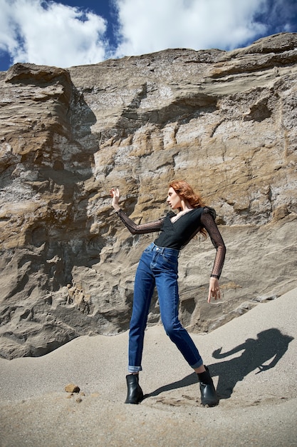 Mode femme rousse posant dans la nature près des rochers de sable. Cheveux longs bouclés et maquillage naturel