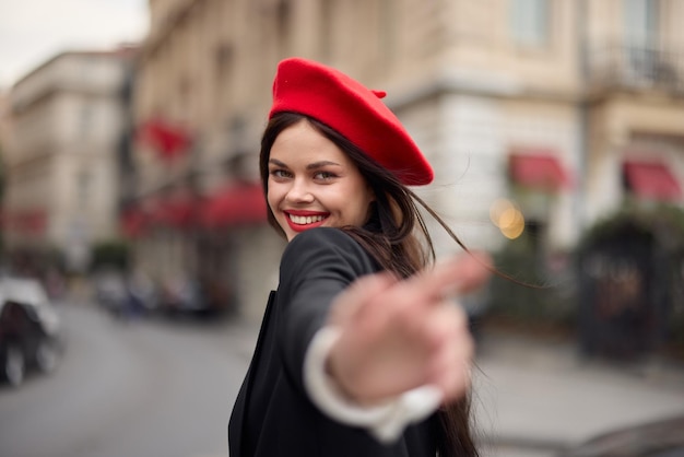 Mode femme sourire avec des dents debout dans la rue devant le touriste de la ville suivez-moi des vêtements élégants avec des lèvres rouges et un béret rouge voyage cinématographique couleur rétro style vintage mode urbaine