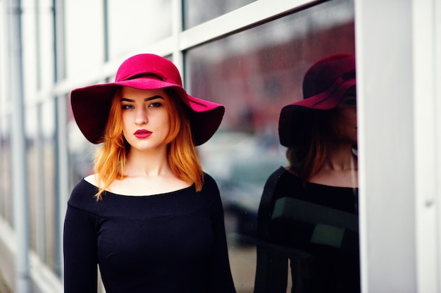 Mode fille aux cheveux rouge sur un chapeau rose et une robe noire avec lumineux font sur une grande fenêtre