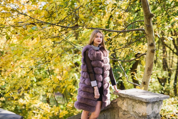 La mode habille la femme en manteau de fourrure et robe posant dans le parc d'automne