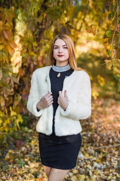 La mode habille la femme en manteau de fourrure et robe posant dans le parc d'automne