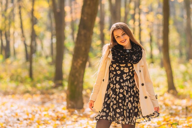 Mode jeune femme dans une jolie robe, manteau blanc et écharpe debout dans le parc automne.