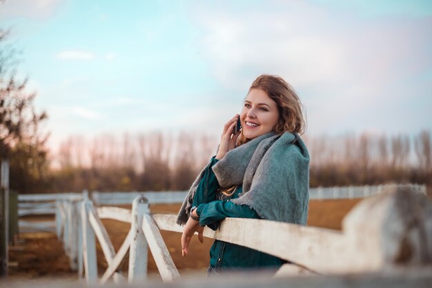 À la mode jeune femme se penchant sur la clôture et parler au téléphone.