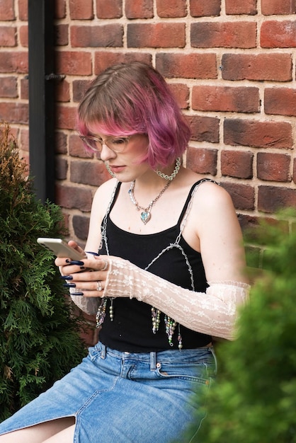 Photo mode jeune fille créative cheveux de couleur rose debout au mur de briques avec smartphone