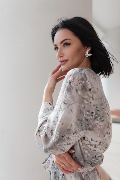 Mode jolie femme européenne modèle avec un visage de beauté en robe vintage élégante avec des stands de motifs de fleurs et pose près d'une colonne blanche dans la rue