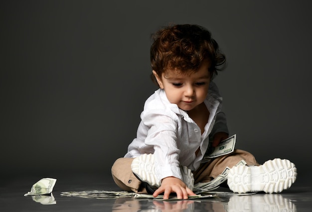 Mode petit bébé patron et argent Petit enfant en bas âge jouant en comptant la monnaie des billets en espèces Portrait isolé isolé sur fond gris studio Allocation et finances des enfants