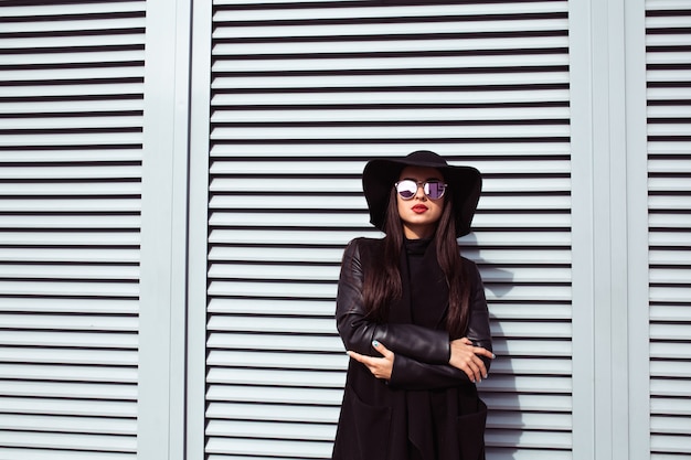 Mode portrait d'une belle femme brune à lunettes et chapeau posant devant les volets de la ville