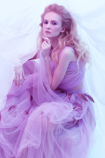 Mode portrait de la belle jeune femme en robe violette moelleuse. Cheveux bouclés blonds, maquillage, robe à plumes, couleurs douces, photo d'art