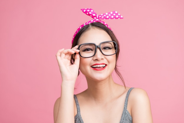 Mode portrait d'une fille asiatique avec des lunettes de soleil debout sur fond rose.